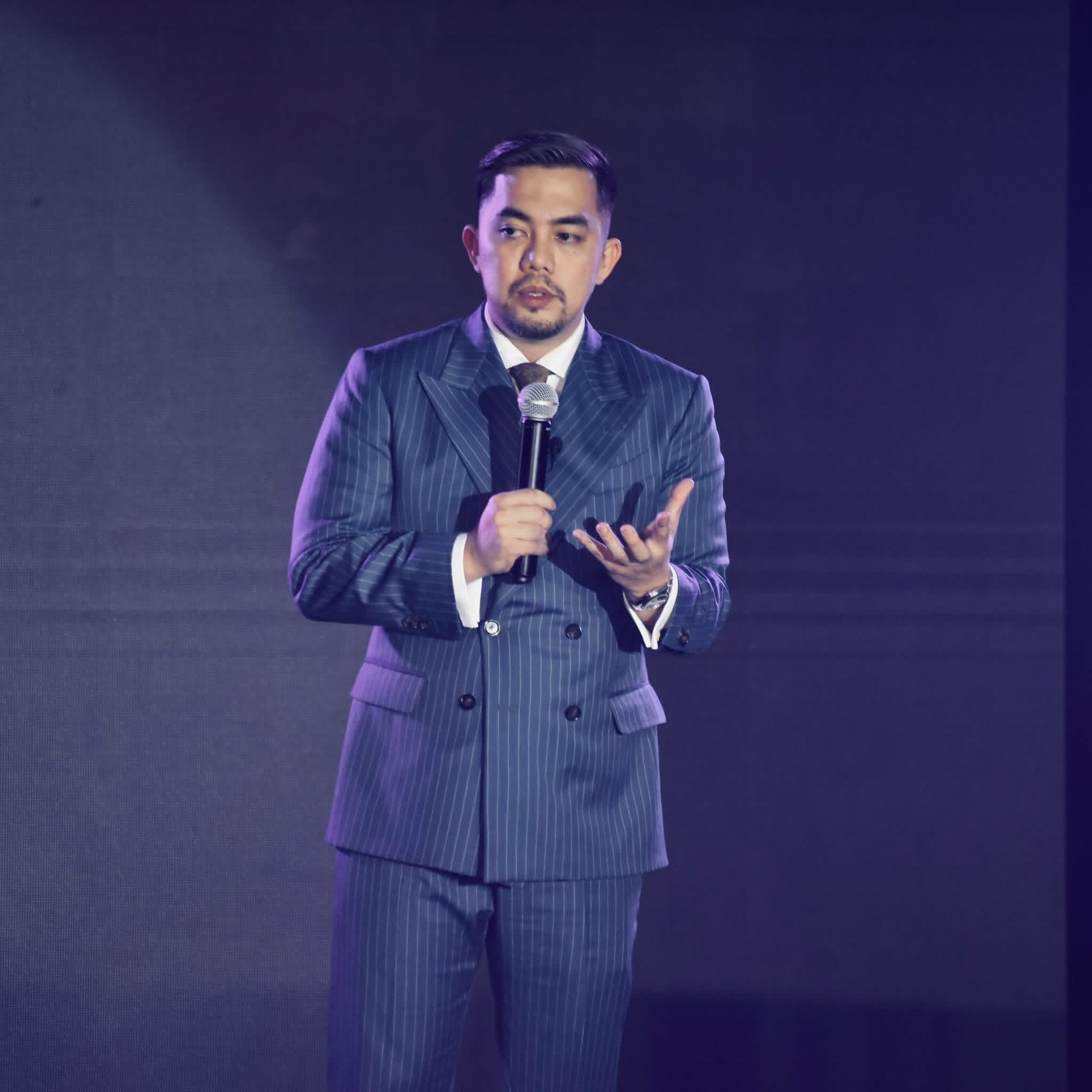 Reymond delos Reyes on stage in a purple pinstripe suit, delivering a keynote speech